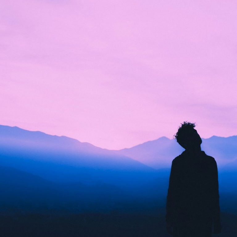 Eine Person sieht in den Himmel. Vernebelte Berge im Hintergrund, violettes und blaues Licht Eine Person sieht in den Himmel. Vernebelte Berge im Hintergrund, violettes und blaues Licht